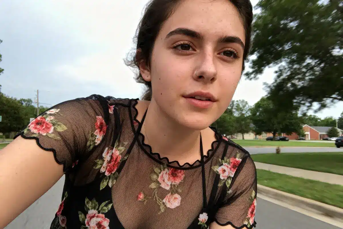 Young woman with floral top biking on suburban street, trees and houses in background, focused expression.