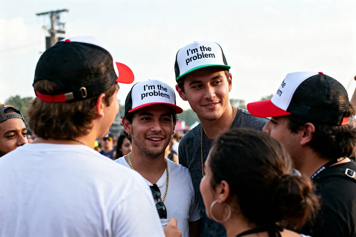 A group of people outdoors, wearing hats with the text "I'm the problem" at a social gathering.