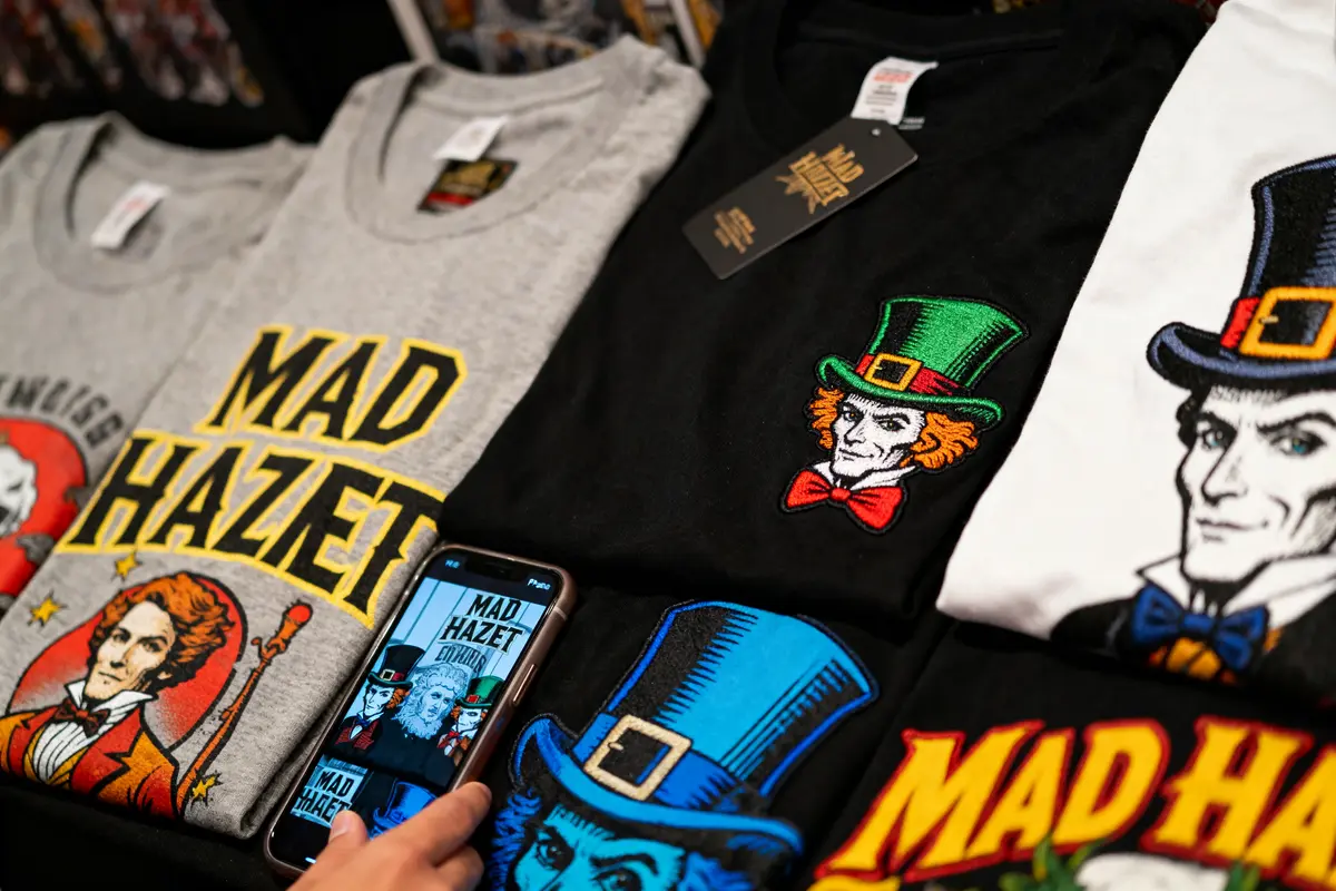 Various graphic t-shirts featuring cartoon characters and "Mad Hazet" text, with one shirt captured on a smartphone screen.