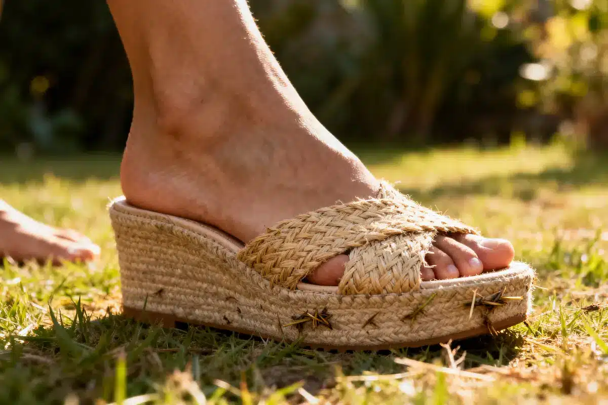 Close-up of a person's foot wearing woven straw platform sandal with grass caught in it.