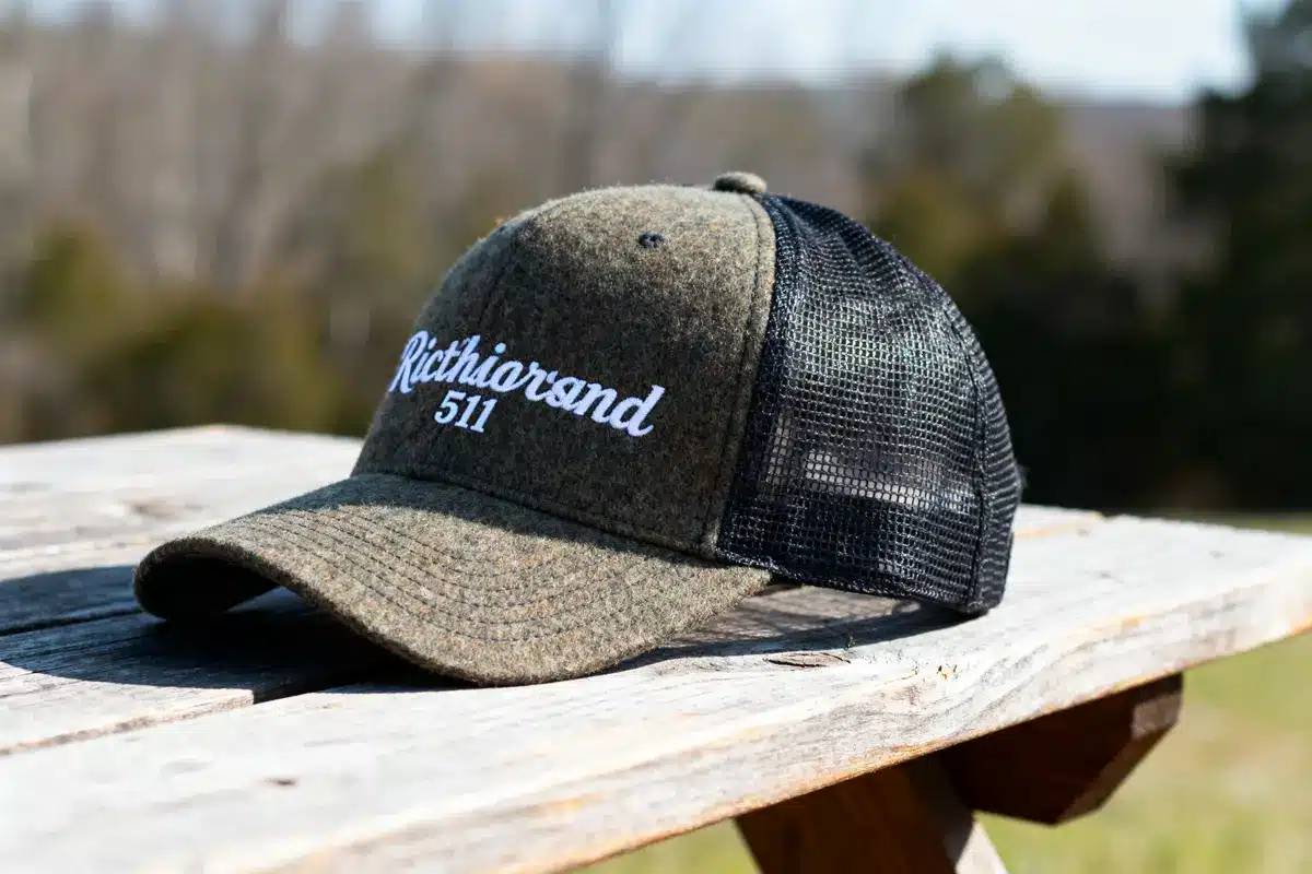 A mesh trucker hat on a wooden table, with "Richiarsand 511" embroidered, outdoors.