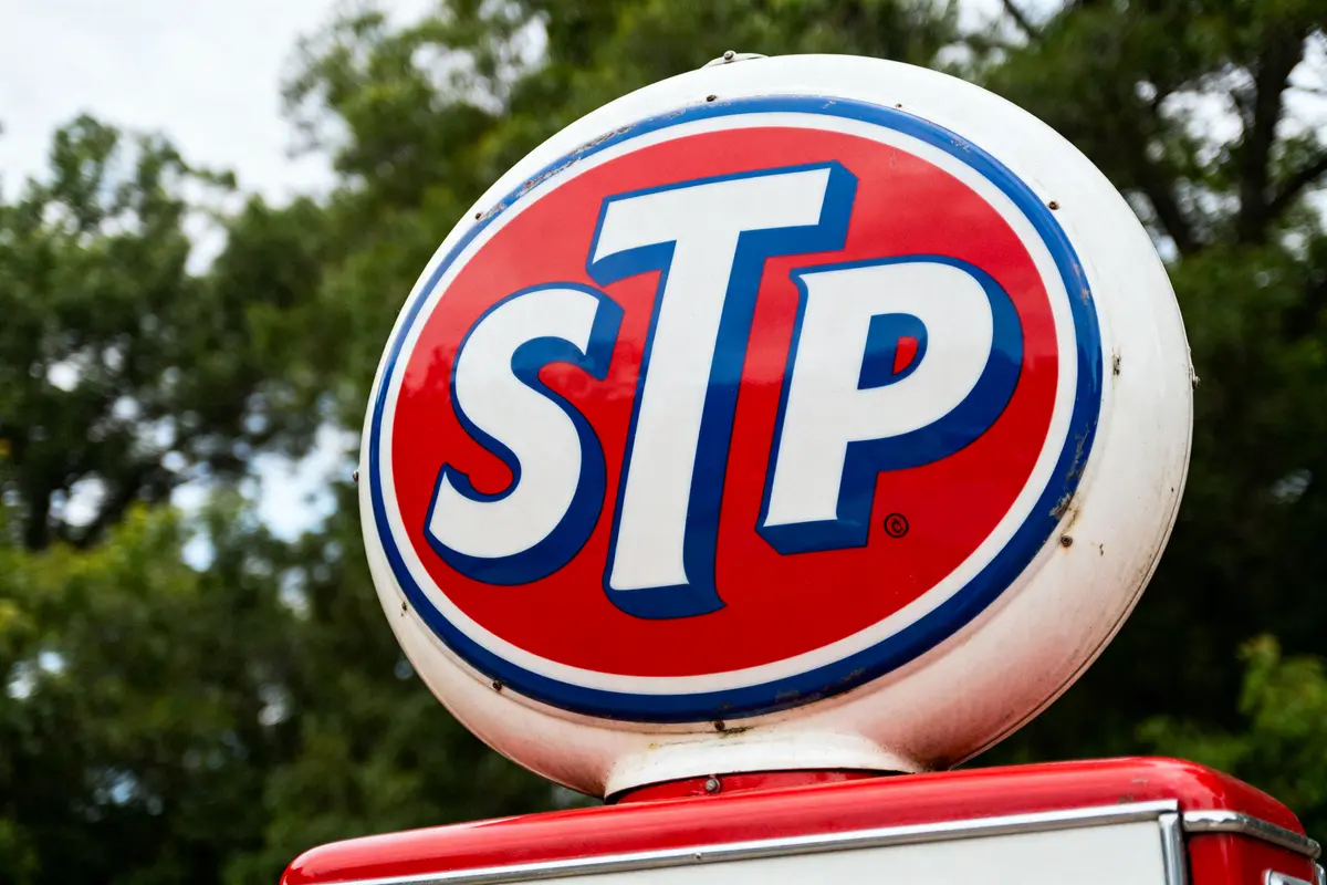 Red and white STP sign against blurred green foliage background.