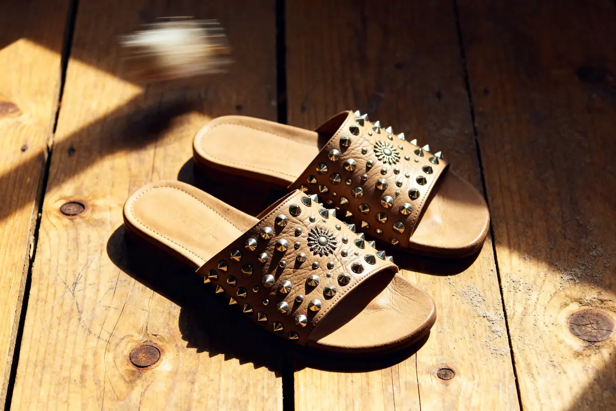 Brown studded sandals with decorative embellishments on a wooden floor, captured in warm natural light.