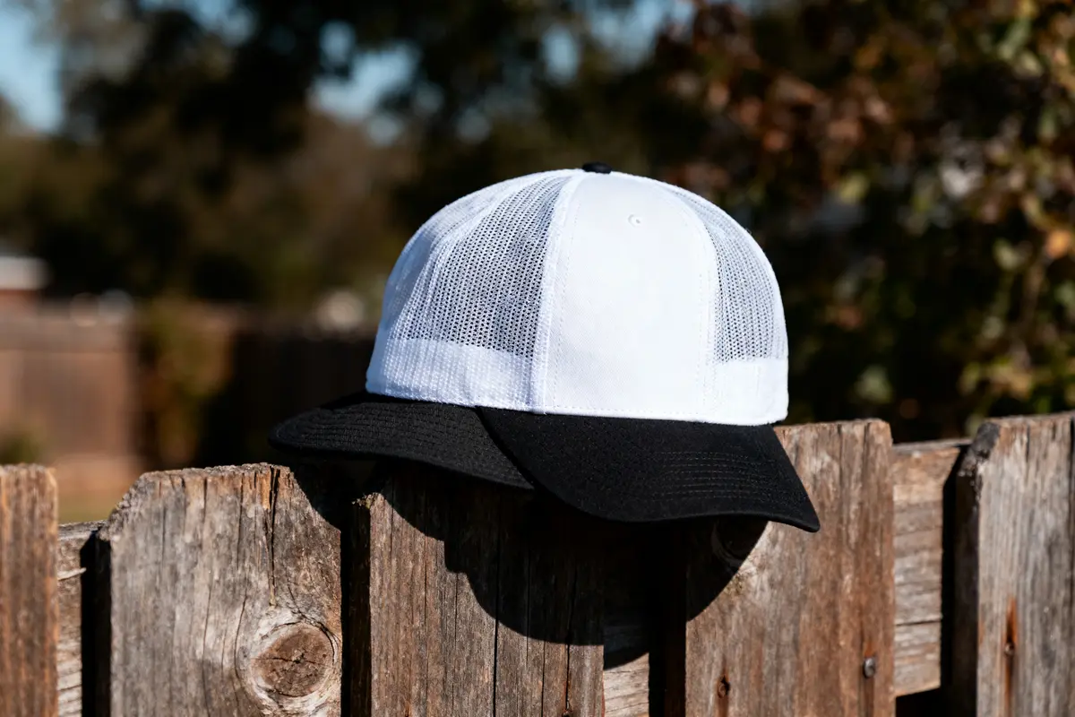 White and black mesh cap resting on wooden fence, with blurred natural background in sunlight.